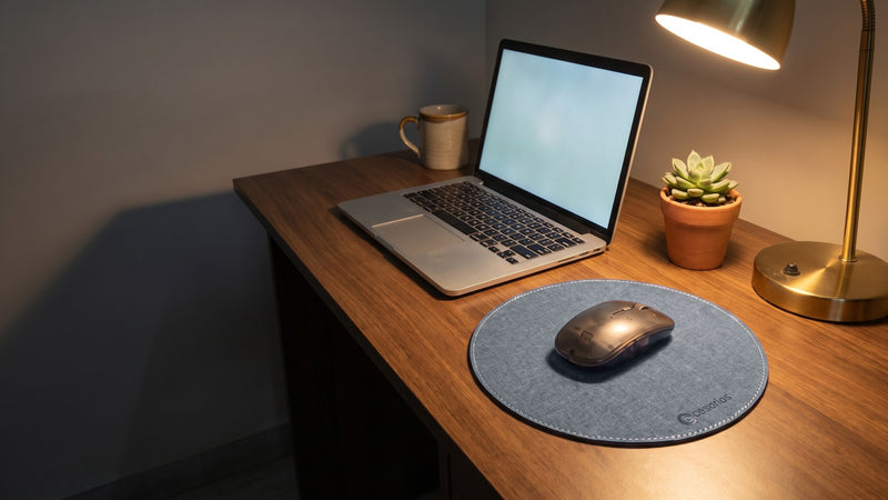 The round mouse pad on a desk beside a laptop, a mug, a plant and a lamp