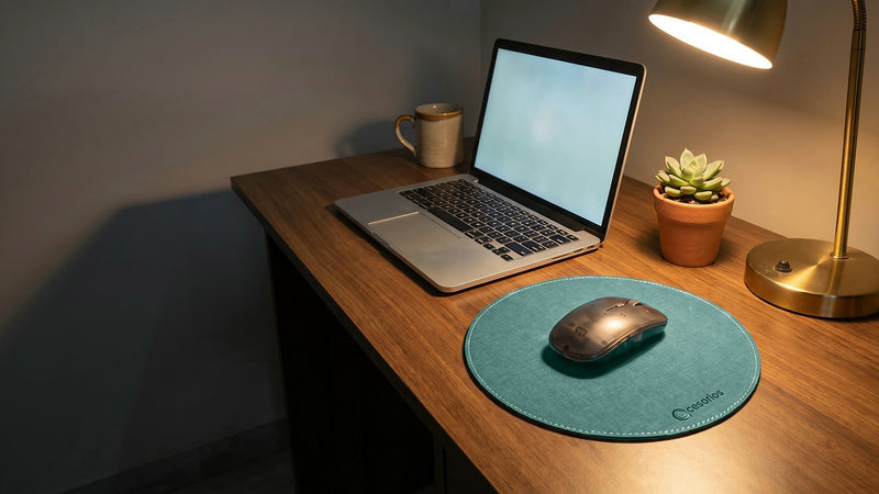 The round mouse pad on a desk beside a laptop, a mug, a plant and a lamp