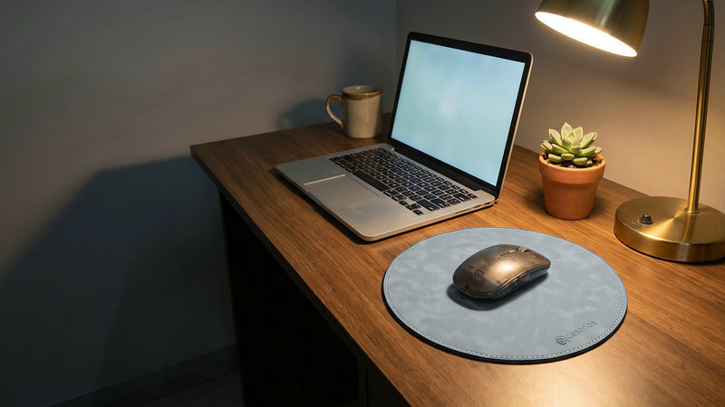 The round mouse pad on a desk beside a laptop, a mug, a plant and a lamp