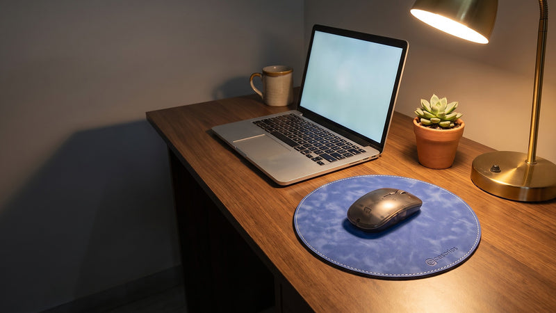 The round mouse pad on a desk beside a laptop, a mug, a plant and a lamp
